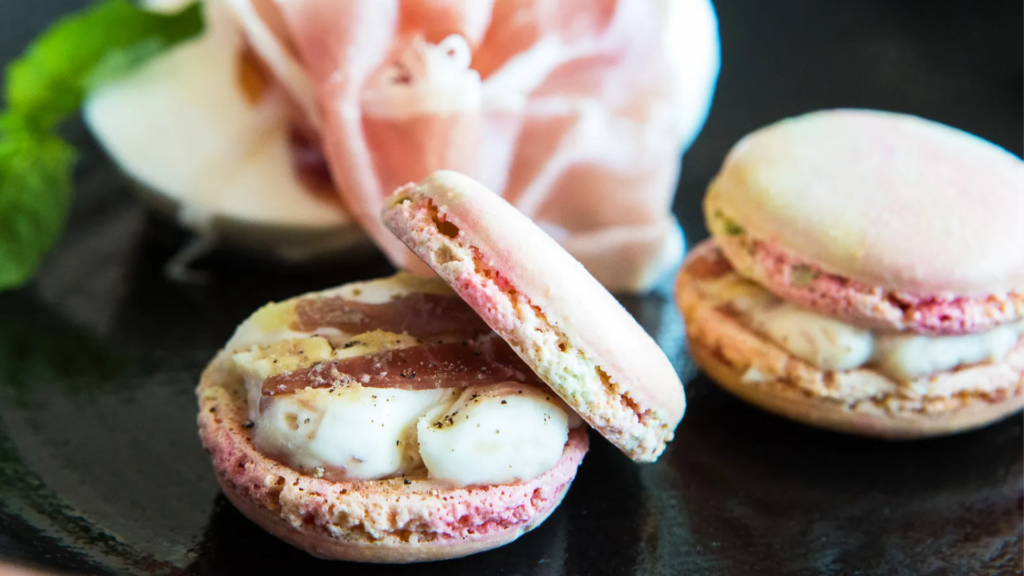 Close up of savoury pink macarons filled with soft cream, arranged on a dark plate with shallow depth of field
